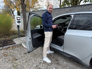 Elektroauto-Unfall in Erding – Ihr Kfz-Gutachter mit Hochvolt-Kompetenz: Andreas Anzer bei einem Gutachten Elektroauto. silbernes Elektroauto an eine Ladestation